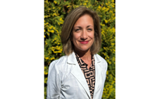 Dr. Narr stands in front of green plants and flowers in her white coat. 